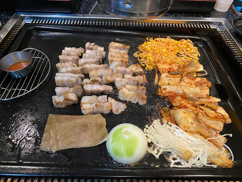 잘 구워진 삼겹살과 김치, 콩나물, 버섯, 양파가 놓인 불판