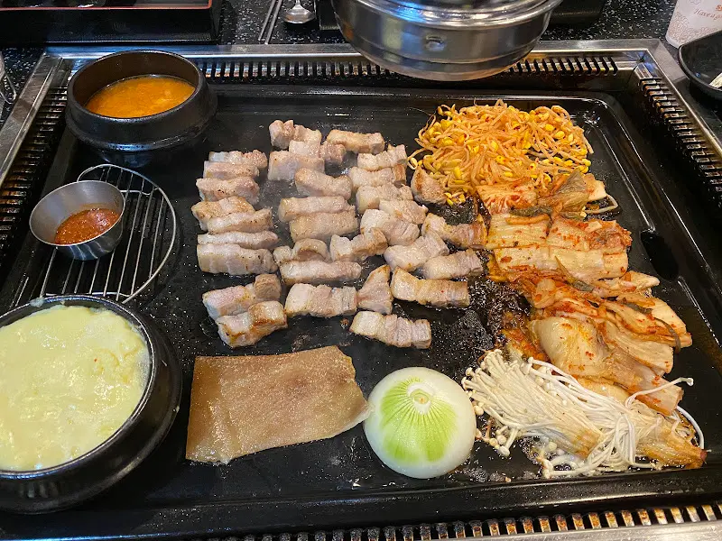 불판 위에 푸짐하게 구워진 삼겹살과 곁들임 채소들