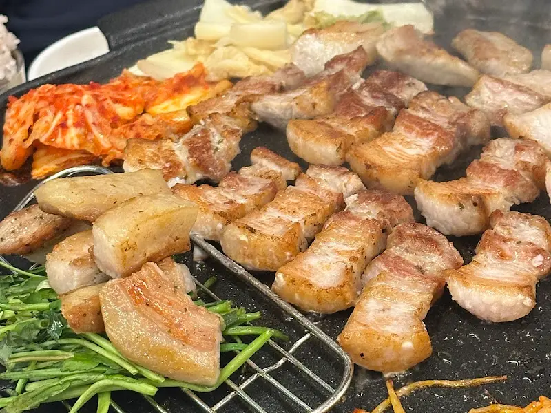 잘 구워진 삼겹살과 구운 김치가 솥뚜껑에 놓여있는 모습