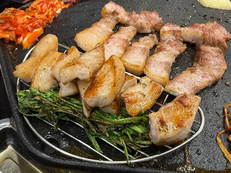 잘 구워진 삼겹살과 멜젓이 솥뚜껑에 올려져 있는 모습