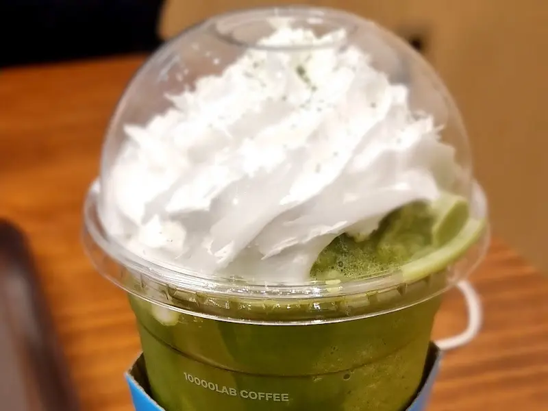 말차 프라페의 클로즈업 사진. 컵 가득 담긴 프라페 위에 휘핑크림이 듬뿍 올려져 있고, 말차 가루가 뿌려져 있다.