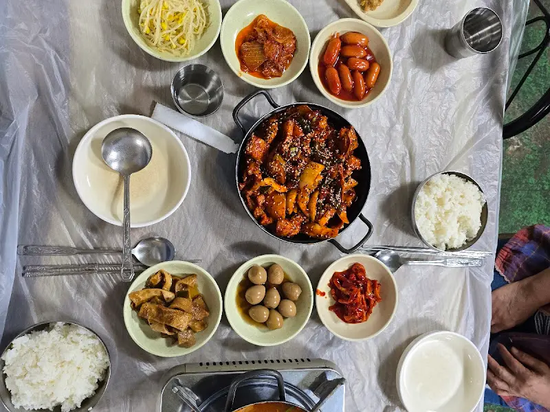 두루치기, 김치찌개, 콩자반, 소시지 등 다양한 밑반찬이 차려진 테이블 전경