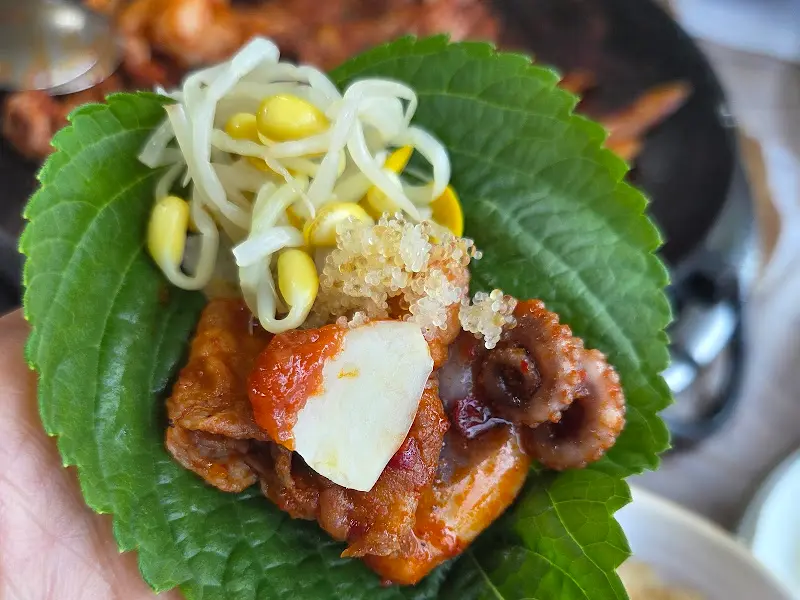 깻잎 위에 쭈꾸미, 삼겹살, 새우, 쌈무, 콩나물을 올려 크게 싼 쌈