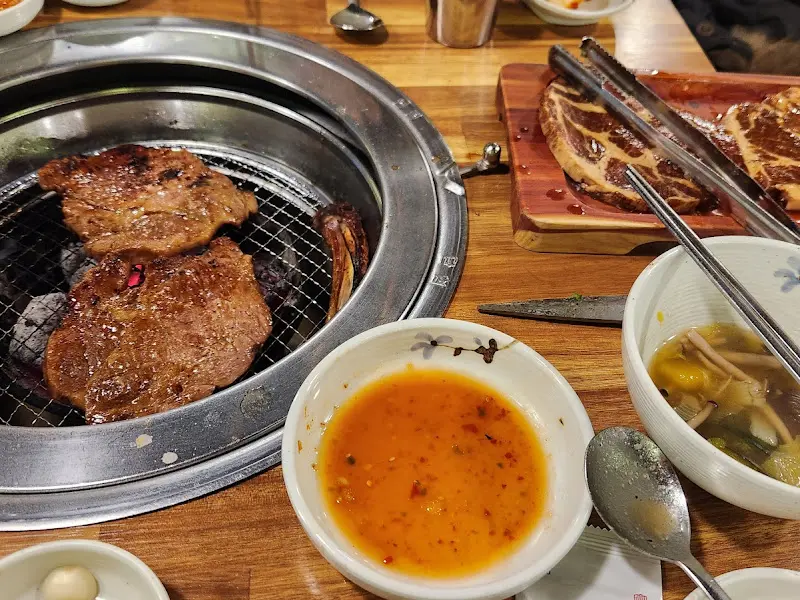 숯불 위에서 맛있게 익어가는 돼지갈비. 곁들여 먹을 수 있는 양파절임과 소스가 함께 놓여 있다.