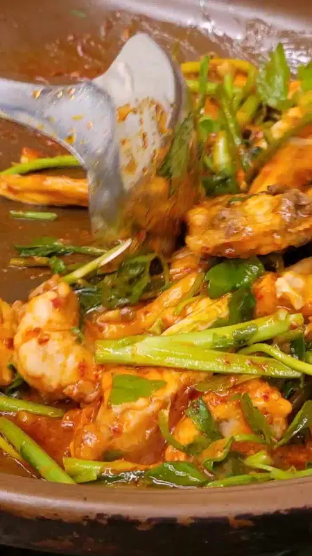 붉은 양념에 버무려진 복어와 미나리가 냄비 안에서 조리되고 있다. 국자로 재료를 섞는 모습이 보인다.