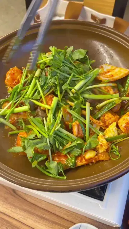 갈색 냄비 안에서 복불고기가 익어가고 있으며, 집게로 재료를 섞고 있다.