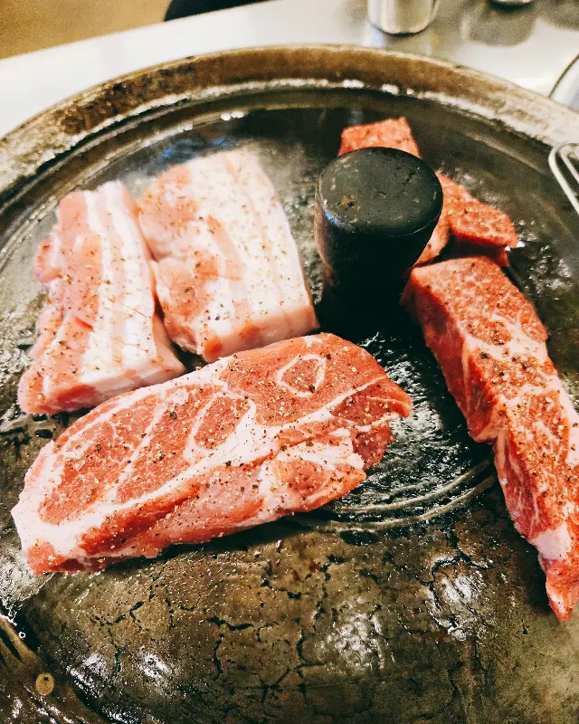 솥뚜껑 위에 가지런히 놓인 삼겹살과 목살