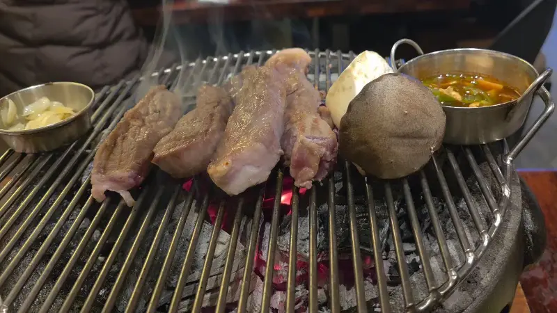 숯불 위에서 익어가는 숙성 목살과 새송이버섯