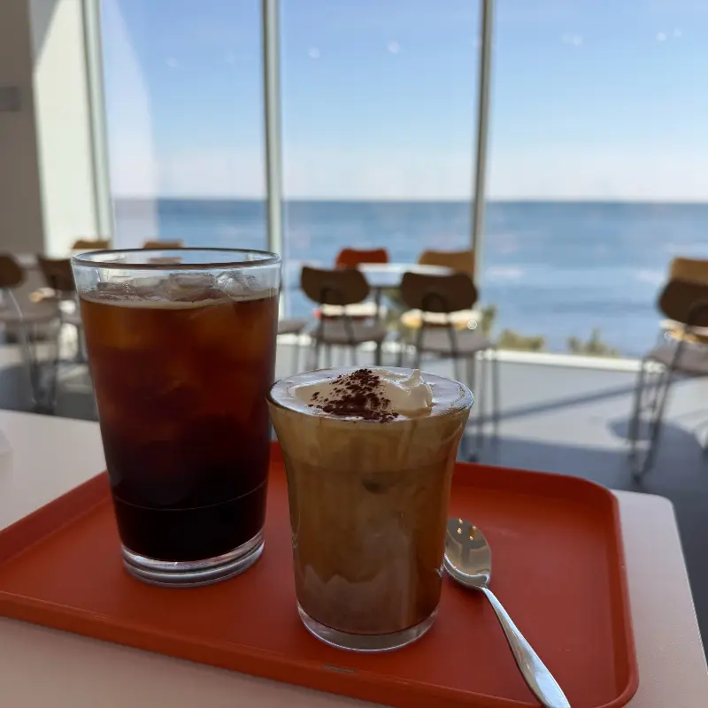 통창으로 보이는 바다를 배경으로 놓인 음료 두 잔