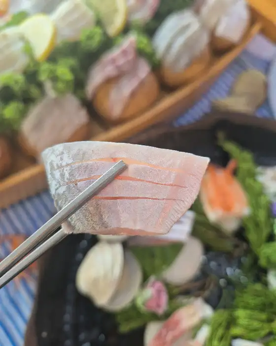 집게로 집어 올린 신선한 활어회 한 점