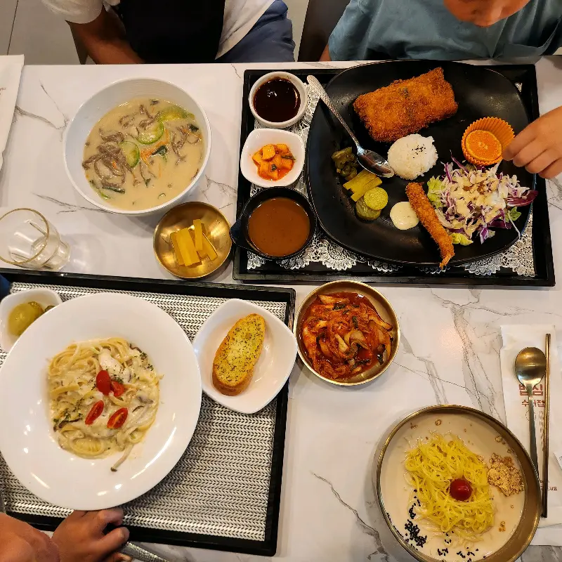 테이블 위에 놓인 돈까스, 파스타, 콩국수의 모습