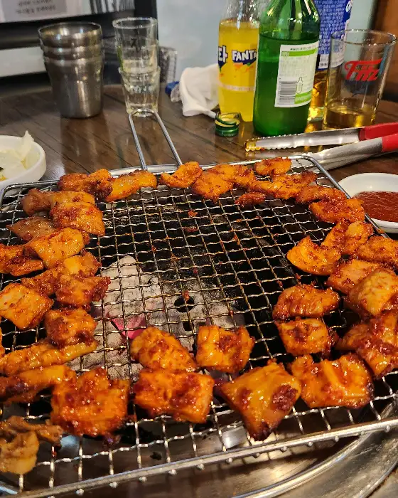 숯불 위에서 다양한 크기와 모양으로 구워지고 있는 막창들. 붉은 양념이 먹음직스럽다.