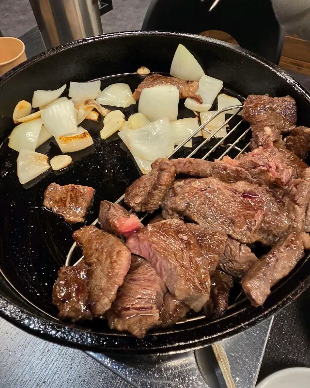 무쇠 팬에 담긴 등심과 구운 마늘, 양파