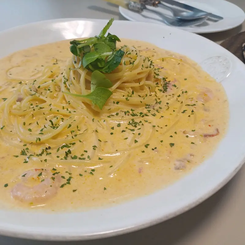 접시에 담긴 크림 파스타 위에 녹색 채소가 올려져 있다