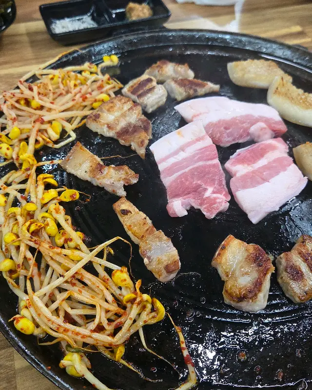 불판 위에서 삼겹살과 콩나물이 함께 구워지고 있는 모습