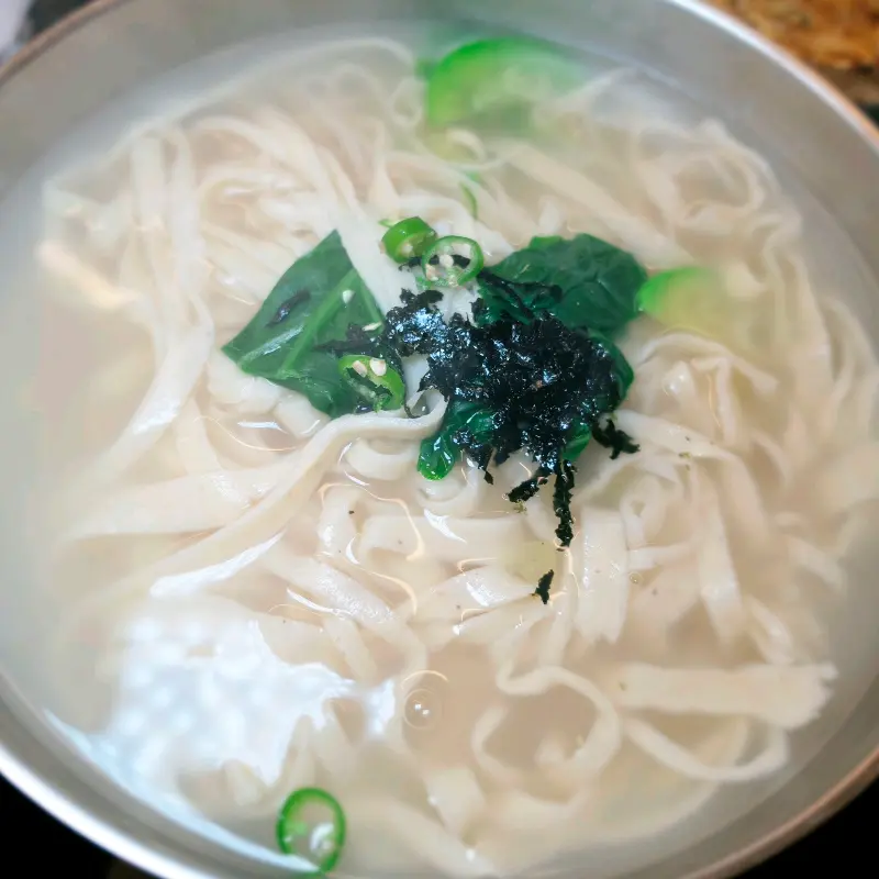 뽀얀 국물에 김가루와 채소가 얹어진 칼국수의 모습