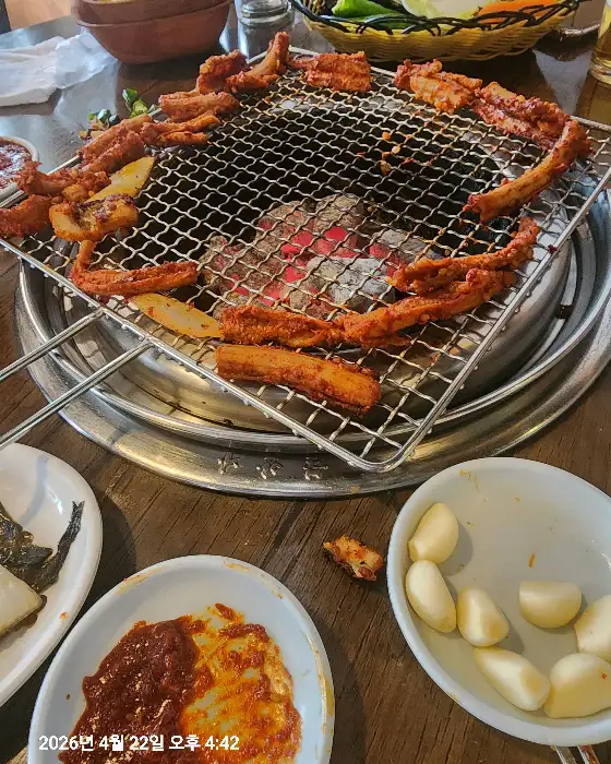 테이블 중앙의 숯불 위에서 꼼장어가 구워지고 있는 모습. 붉은 양념이 먹음직스럽게 배어 있다.