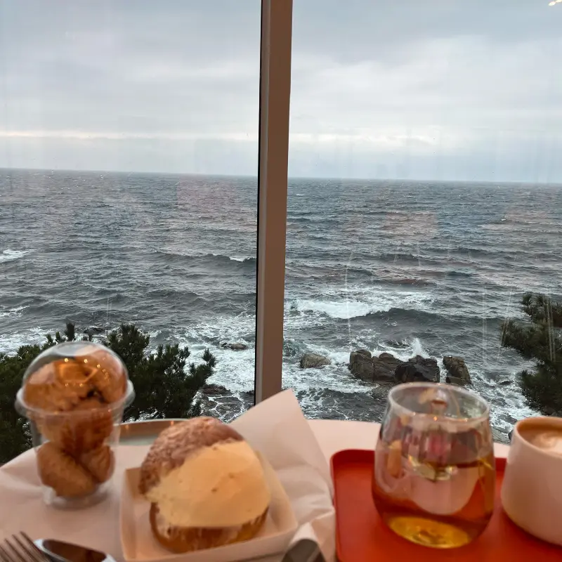 창밖의 바다를 배경으로 놓인 바닐라빈 라떼와 소금빵