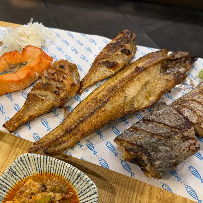 테이블 위에 차려진 푸짐한 생선구이와 다양한 밑반찬 모습. 고등어, 연어, 갈치 등 여러 종류의 생선구이가 먹음직스럽게 담겨 있다.