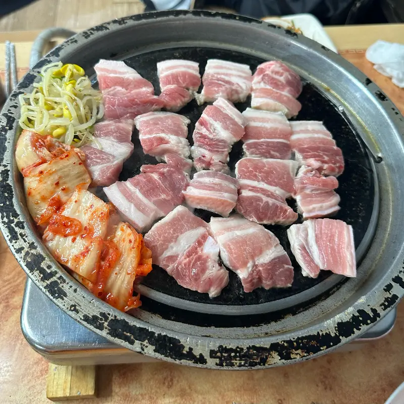 불판 위에 김치와 콩나물을 올려 삼겹살과 함께 구워먹는 모습