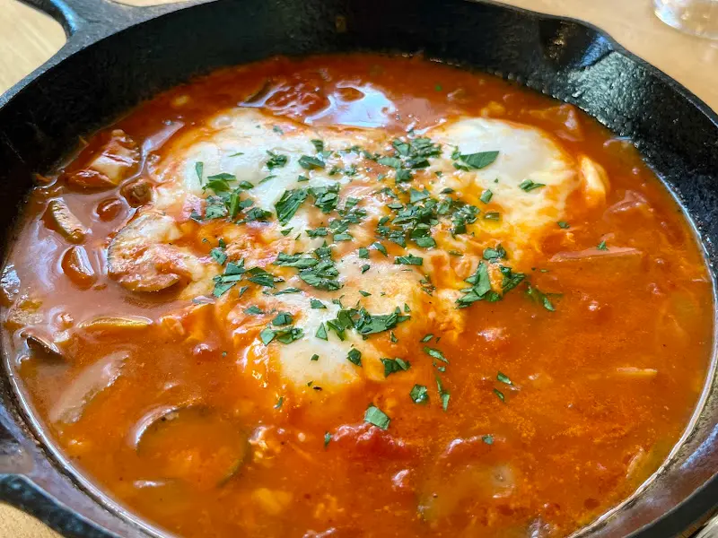 무쇠 팬에 담긴 샥슈카. 토마토 소스 베이스에 반숙 계란이 얹혀 있고, 파슬리가 뿌려져 있다.