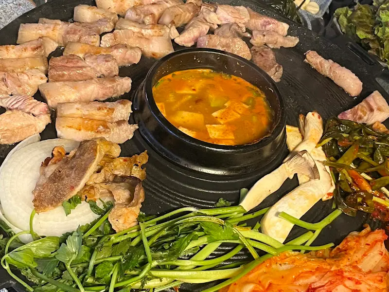 솥뚜껑에 가득찬 삼겹살, 김치, 콩나물, 미나리