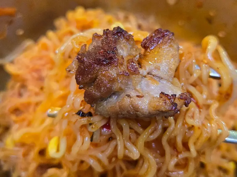 비빔면에 올려진 돼지고기 한 점