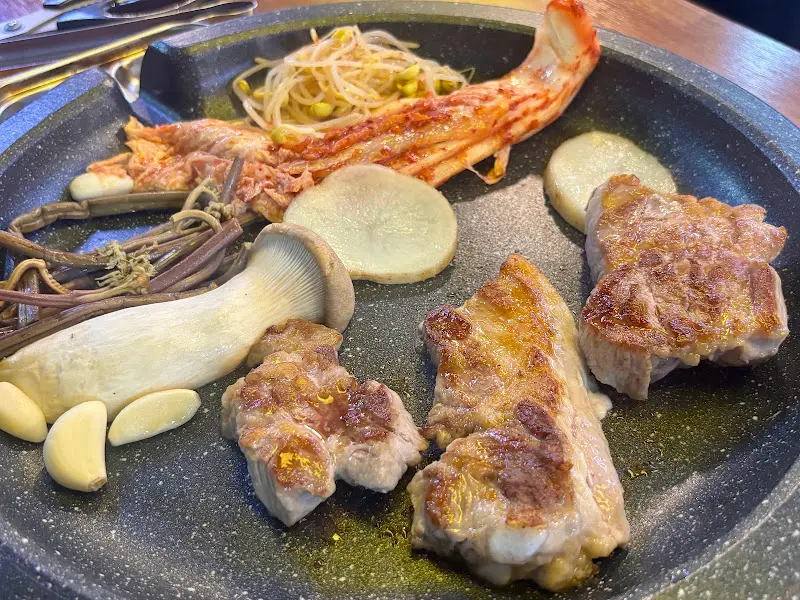 초벌된 돼지고기, 버섯, 김치, 콩나물이 불판 위에 올려져 있는 모습