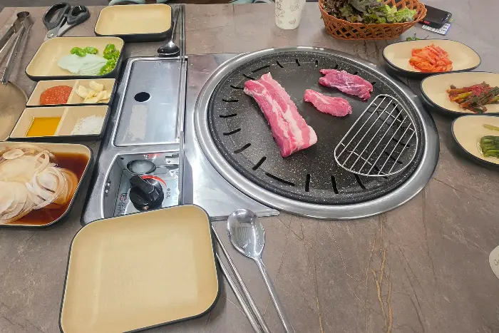 신선한 돼지고기, 쌈 채소, 김치, 마늘 등이 준비된 테이블