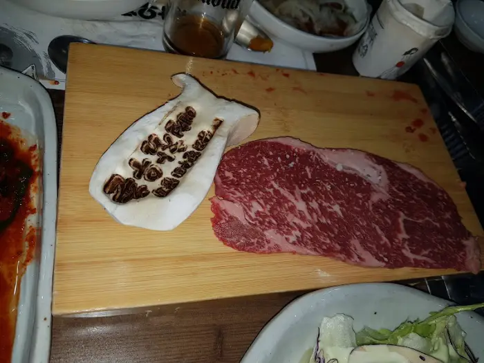 먹음직스럽게 썰린 신선한 생고기와 버섯 조각이 나무 도마 위에 놓여 있다.