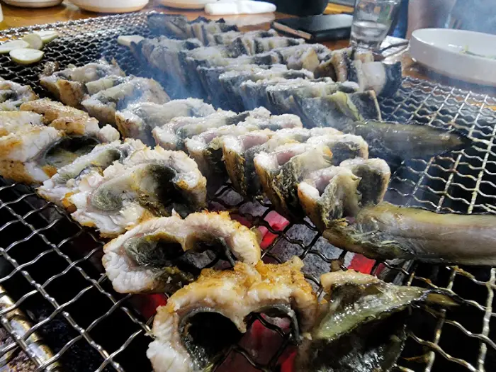 숯불 위에서 익어가는 장어와 함께 다양한 반찬이 테이블에 놓여 있습니다.