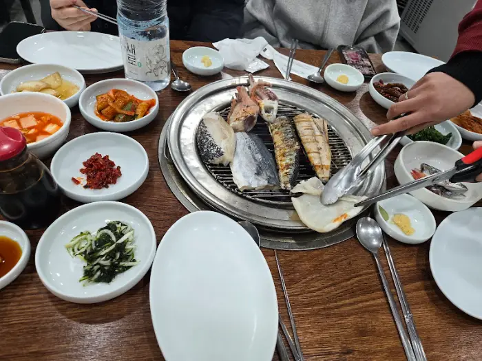 테이블 위에 놓인 다양한 반찬들과 숯불 위 생선구이