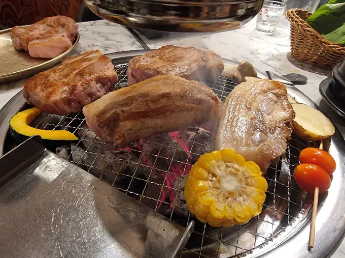 숯불 위에서 맛있게 구워지고 있는 삼겹살과 목살, 옥수수, 토마토