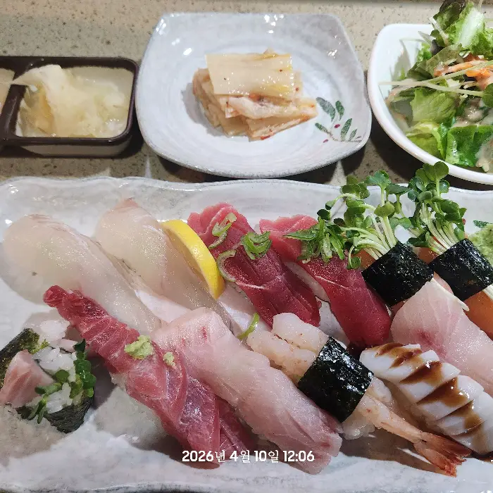 다양한 종류의 초밥이 접시에 먹음직스럽게 담겨 있고, 곁들임 음식들이 함께 놓여 있는 모습