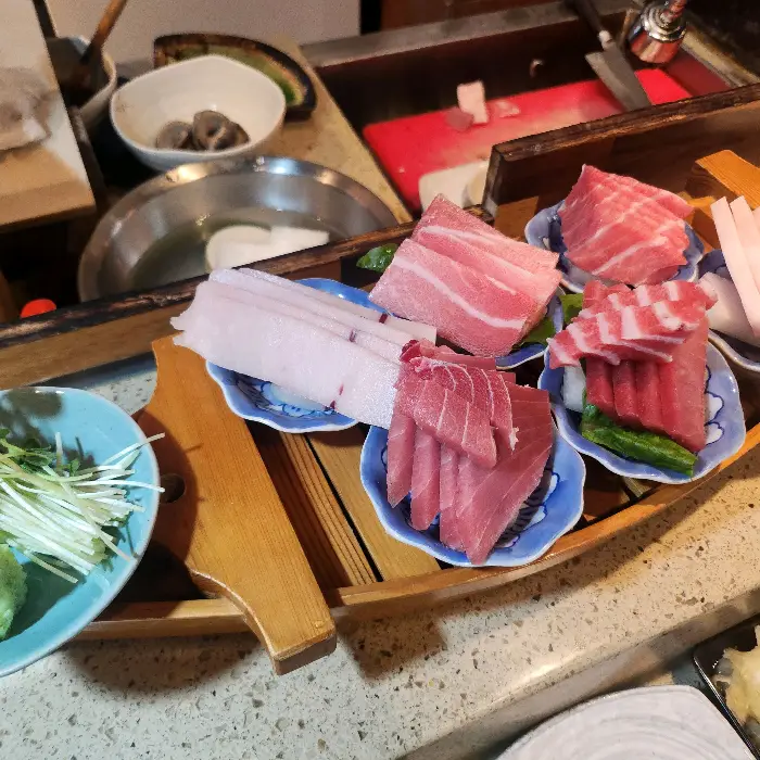 나무 접시에 여러 종류의 참치회와 곁들임 채소가 놓여 있는 모습