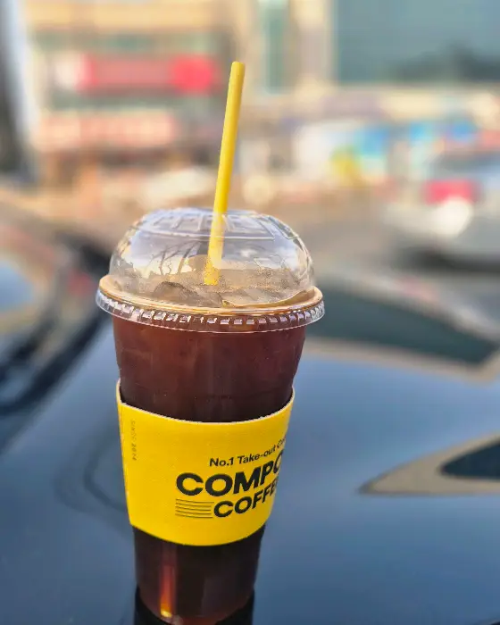 차량 위에 놓인 아이스 아메리카노 컵, 배경에는 컴포즈커피 매장이 보임