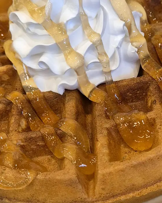 따뜻하게 구워진 와플 위에 휘핑크림과 시럽이 뿌려진 모습