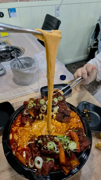 치즈를 듬뿍 뿌린 뼈구이 위에 집게로 치즈를 늘어뜨리는 모습