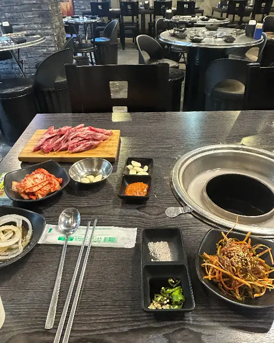 테이블 위에 차려진 다양한 밑반찬들과 고기, 그리고 숯불구이 불판