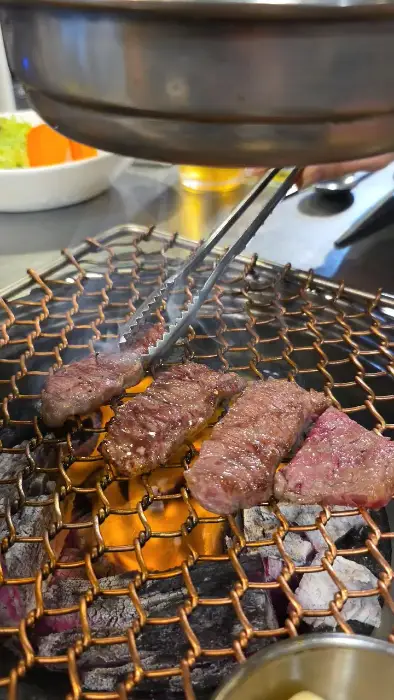 집게로 소고기 조각을 집어 숯불 위로 옮기는 모습