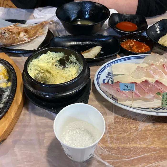 테이블에 놓인 다양한 해산물 요리, 연어, 계란찜, 물회 등