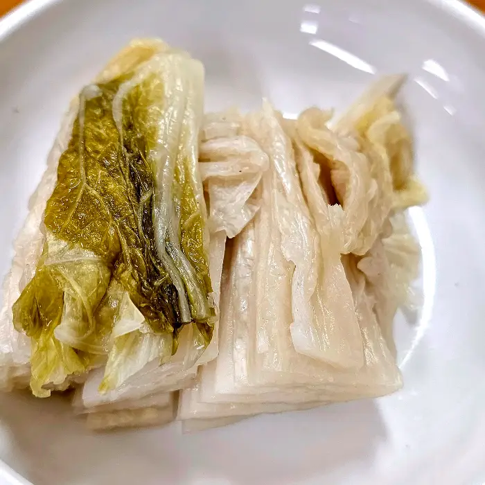 하얗게 익은 배추김치 잎사귀가 접시에 담겨 있습니다. 맑고 깨끗한 느낌을 줍니다.