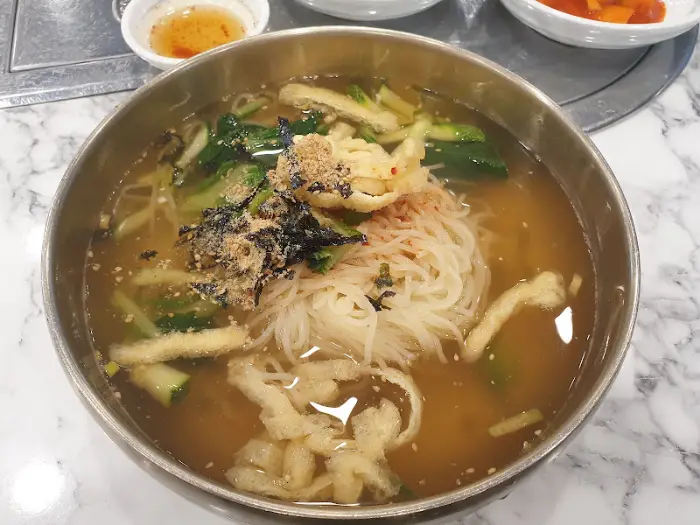 국수 메뉴의 클로즈업. 얇은 면발과 맑은 육수가 보인다.