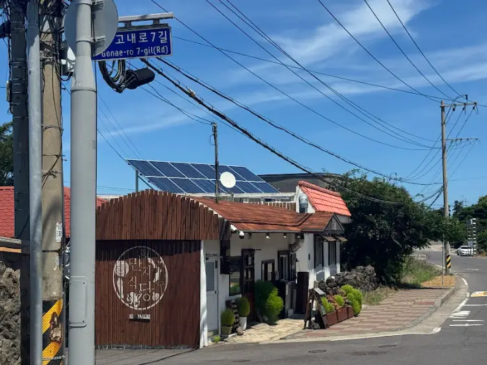 가게 외부 전경. 작은 건물에 아기자기한 간판이 걸려 있고, 주변에 푸른 나무들이 있어 정겨운 느낌을 준다.