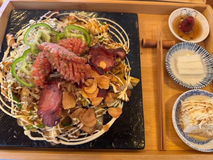 돈까스와 야끼소바의 클로즈업 사진. 돈까스는 두툼하고 바삭해 보이며, 야끼소바에는 다양한 재료가 풍성하게 올라가 있다.