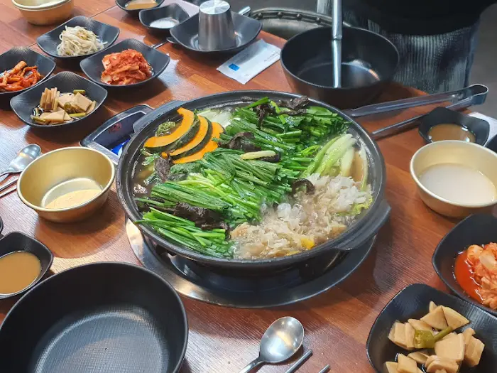 테이블 위에 놓인 닭백숙 냄비와 여러 반찬들. 냄비 안에는 닭고기와 함께 단호박, 배추, 파 등이 푸짐하게 들어있다.