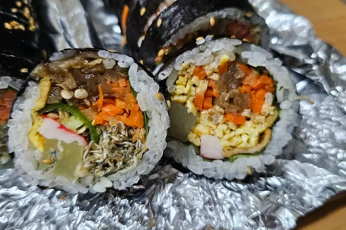 김밥의 단면이 보입니다. 밥 위에 다양한 재료들이 층층이 쌓여 있습니다.