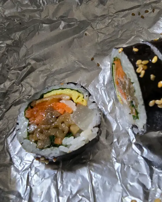 김밥 단면 사진. 밥 위에 멸치볶음, 당근, 계란지단 등이 보입니다.