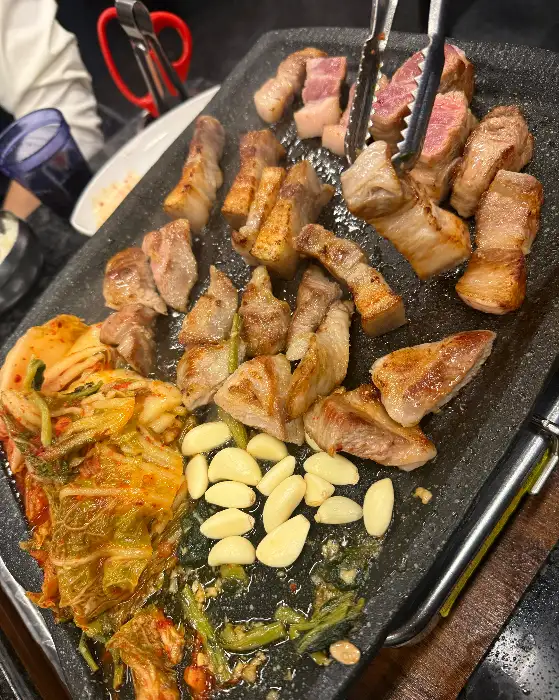 삼겹살, 김치, 마늘, 콩나물이 함께 구워지는 모습