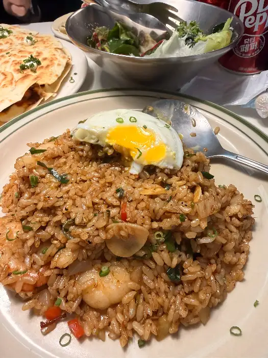 풍성한 새우와 채소가 볶아진 밥 위에 반숙 계란 프라이가 올라간 덮밥 메뉴.